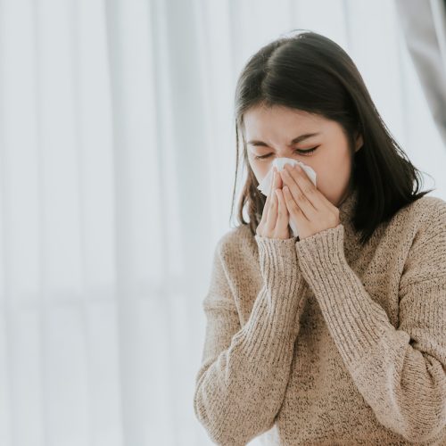 Sick Asian woman using a tissue to sneeze and blowing her nose in winter at home. Her getting sick with flu and cold.